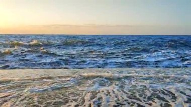 Gün batımında fırtına. Denizde fırtına. Beyaz köpüklü büyük açık deniz dalgaları beton iskele duvarına çarpıyor ve güneşli yaz gününde su sıçrıyor. Fırtınalı deniz. Dalgalı deniz. Kıyıya. Doğa. Doğal arkaplan