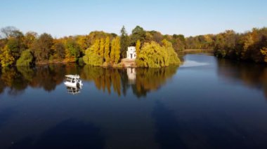 Lake,smooth mirror water surface, white boat, trees yellow leaves, architecture, blue sky, park on autumn sunny day. Nature background. Natural scenery. Aerial Beautiful autumn landscape. Environment
