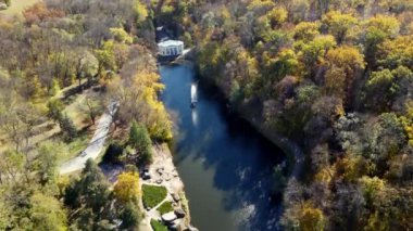 Sonbaharda park et. Gölü, çeşmesi, yolları, sarı yapraklı ağaçları ve güneşli bir sonbahar gününde yürüyen insanları olan güzel bir parkın manzarası. Hava aracı görüntüsü. Doğa. Doğal arkaplan