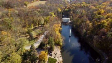 Sonbaharda park et. Gölü, çeşmesi, yolları, sarı yapraklı ağaçları ve güneşli bir sonbahar gününde yürüyen insanları olan güzel bir parkın manzarası. Hava aracı görüntüsü. Doğa. Doğal arkaplan