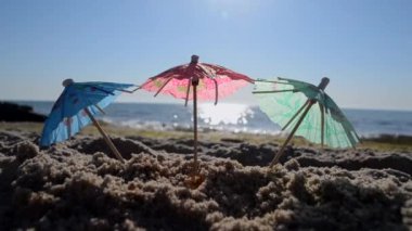 Güneşli yaz gününde, kumsalda, kumsalda kağıt kokteyl şemsiyeleri. Deniz kıyısında deniz kenarındaki şemsiyeler. Üç küçük şemsiye, deniz dalgalarının kumlu arka planında duruyor.