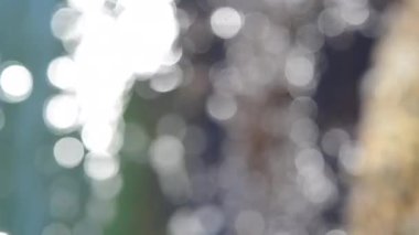 Deniz dalgaları yuvarlanıyor ve kayalara çarpıyor. Suyun yüzeyinde bir sürü beyaz güneş lekesi parlıyor. Güneşli yaz gününde deniz manzarası. Bulanık soyut doğal arkaplan dikey