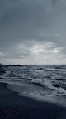 Fırtınalı havalarda kumsaldaki kumsallar, gök gürültülü bulutlar ve deniz yüzeyindeki yağmurlar. Denizde fırtına. Gökyüzünde yağmur bulutları. Kumlu sahilde dalgalar akıyor. Doğa. Doğal arka plan. Dikey