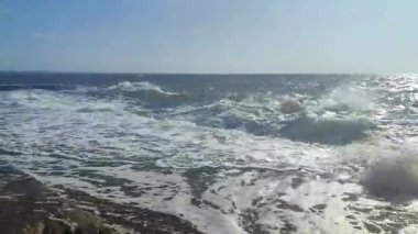 Güneşli bir yaz gününde denizde fırtına. Güneşli bir günde beton eski iskeleye beyaz köpüklü büyük deniz dalgaları çarpıyor. Çimento iskelesine ve temiz mavi gökyüzüne çarpan büyük dalgalardan bir sürü sıçrama.