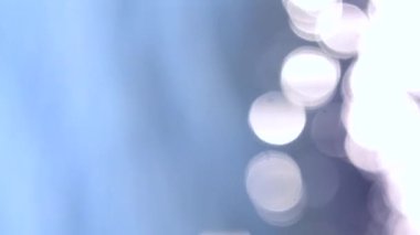 Güneşli yaz gününde deniz manzarası. Deniz Burnu. Mavi deniz suyu yüzeyli deniz manzarası, küçük dalgalanmalar, beyaz bokeh noktaları ve güneşi yansıtan parlak noktalar. Bulanık soyut doğal arkaplan dikey