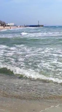 Deniz kıyısında. Kumsalda mavi deniz dalgaları ve beyaz deniz köpüğü. Deniz kıyısındaki insanlar. Deniz kıyısında. Deniz kenarında. Güneşli bir yaz gününde deniz manzarası. Deniz manzarası. Doğa. Doğal arka plan. Dikey