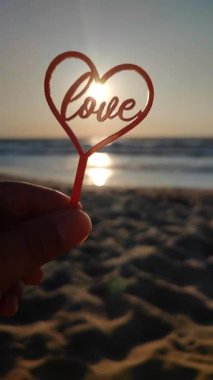 Parmaklarını tutan kişi kırmızı kalbe ve sözcüğe sarılır. Arka planda aşk, deniz ve deniz dalgaları, güneşli yaz günlerinde mavi gökyüzü. Aziz Sevgililer Günü Düşey Aşkı kavramını kabul et