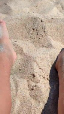 Ayaklarını kuma gömmüş bir kadın. Sıcak yaz gününde kumsalda ayaklarını kuru kuma gömme oyunu oynayan biri. Tatil tatili, dinlenme, dinlenme turizmi, ufalanan dikey