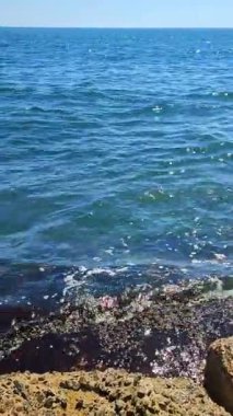 Güneşli yaz gününde kıyıdaki eski taşlardan parlayan beyaz güneşli güzel mavi deniz manzarası. Güzel şeffaf deniz suyu, beyaz güneş lekeleri, beton levhalara çarpan deniz dalgaları.