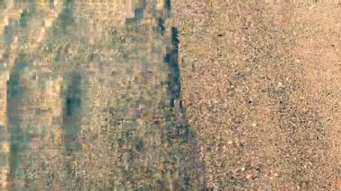 Güneşli bir günde, deniz kıyısının kumsalındaki temiz şeffaf su dalgalarının soyut görüntüsü. Gölgeli dalgalar kumlu bir plaja yakın çekim yapıyor. Güneş kumlu zeminde parlıyor