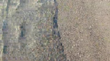 Güneşli bir günde, deniz kıyısının kumsalındaki temiz şeffaf su dalgalarının soyut görüntüsü. Gölgeli dalgalar kumlu bir plaja yakın çekim yapıyor. Güneş kumlu zeminde parlıyor