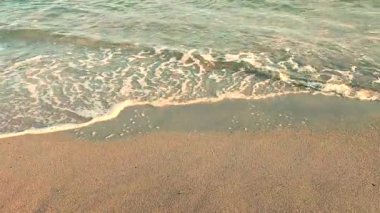 Güneşli bir sonbahar gününde kumlu sahilde beyaz köpüklü deniz dalgaları yuvarlanıyor. Sakin rüzgarsız deniz. Doğa geçmişi. Doğal arkaplan.