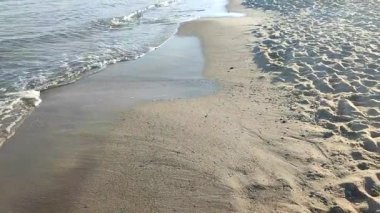 Güneşli bir sonbahar gününde kumlu sahilde beyaz köpüklü deniz dalgaları yuvarlanıyor. Sakin rüzgarsız deniz. Doğa geçmişi. Doğal arkaplan