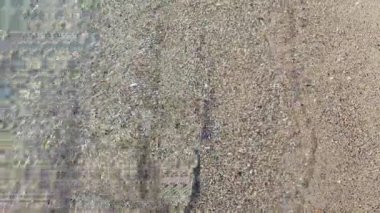 Güneşli bir günde, deniz kıyısının kumsalındaki temiz şeffaf su dalgalarının soyut görüntüsü. Gölgeli dalgalar kumlu bir plaja yakın çekim yapıyor. Güneş kumlu zeminde parlıyor