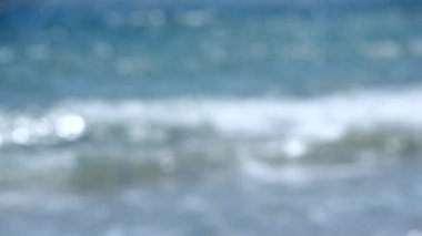 Bulanık arka plan mavi dalgalar beyaz köpükle deniz kıyısında yuvarlanıyor. Güneşin beyaz benekleri deniz dalgalarının üzerinde parlıyor. Deniz mavisi su. Sahil kıyısı Doğal arka plan Doğa
