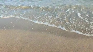 Güneşli bir sonbahar gününde kumlu sahilde beyaz köpüklü deniz dalgaları yuvarlanıyor. Sakin rüzgarsız deniz. Doğa geçmişi. Doğal arkaplan.