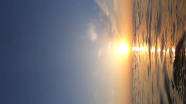 Deniz ve güneş. Dalgalanan dalgalar ve güneşli yollarla deniz suyu yüzeyi. Şafakta ve gün batımında parlayan güneş. Mavi gökyüzü ve beyaz tüy bulutları. Açık gökyüzü denizi. Alt açı. Doğal arkaplan Yavaş çekim Dikey