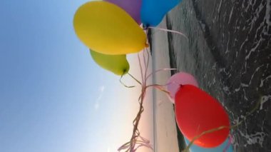 Deniz dalgalarının yakınındaki sahil sahillerinde bir sürü renkli balonla oynayan kişi. Çok renkli küçük balonlar elinde kurdeleyle kumun üzerine bağlanmıştı. Dinlenme eğlencesi şımartma eğlence eğlencesi