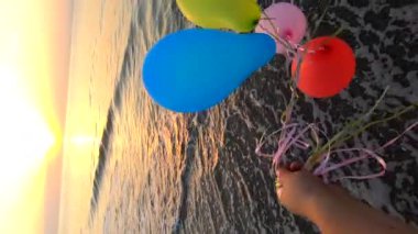 Gün doğumunda ve günbatımında kumlu sahil sahilinde kurdeleyle bağlanmış bir sürü renkli balon ve el. Şafakta çok renkli balonlar. Ağır çekim. Deniz kıyısında, deniz kıyısında. Güneş topların arasından parlar.