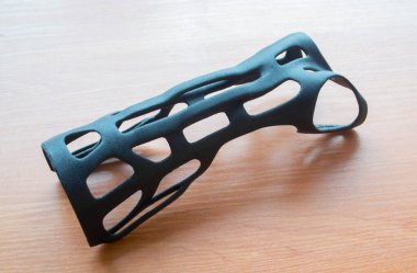 Masadaki erimiş siyah plastik baruttan alınan 3D yazıcıya elle sabitlenmiş korse protezi. Tıbbi ortopedik fiksatör plastik kaplama 3D yazıcıda yaratıldı. Yeni modern tıbbi 3D baskı teknolojisi
