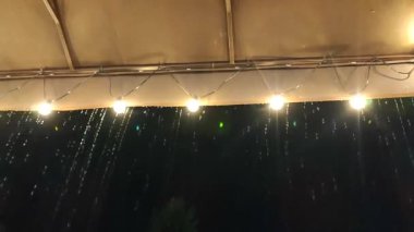 Sarı çatıdan damlayan yağmur damlaları ve gece karanlığında parlayan fenerler. Çatıdan damlayan su damlaları. Alt görünüm