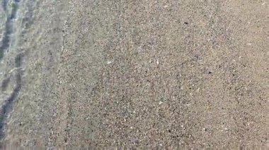 Kumsalda kumsalda yuvarlanan küçük deniz dalgalarının temiz şeffaf sularının soyut görüntüsü. Deniz dalgalarının gölgeleri ve kumlu zeminde su yüzeyinden parlayan güneş. Doğa. Doğal arkaplan