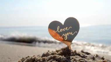 Plastik kalp şeklinde kelimeler. Güneşli yaz günlerinde arka plandaki deniz dalgalarının kumlu sahillerinde seni seviyorum. Aşk ilişkisi romantizmi Aziz Sevgililer Günü kutlaması olarak kabul et.