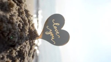 Plastik kalp şeklinde kelimeler. Güneşli yaz günlerinde deniz dalgaları ve kumsaldaki kumsalda seni seviyorum. Aşk ilişkisi aşkı kutlaması Aziz Sevgililer Günü Dikey