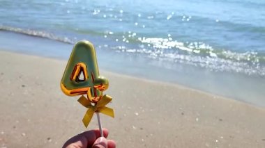 Elinde parlak altın rengi 4 numaralı sopayla elinde sopayla mavi denizin ve güneşli yaz günlerinde kumlu plajların dalgalarına karşı duran kişi. Doğum günü kutlaması kavramı