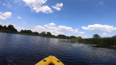 Şişme bir teknede yüzen ve güneşli bir yaz gününde yeşil ağaçlar ve çalılarla küçük bir nehir boyunca kürek çeken kişi. POV kanosu sakin nehirde. Turizm eğlence sektörü