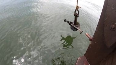 Denizde giden bir geminin gövdesinde sallanan eski bir çapa. Eski paslı çapa ipte sallanıyor ve denizin üstünde yüzen ahşap bir geminin pruvasının yanında sendeliyor. Seyahat turizmi