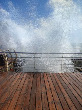 Large wave hitting wooden pier jetty with a lot of splashes on a sunny day. Storm, stormy sea. Weather. Travel, tourism,vacation. Coast, coastal, shore clipart