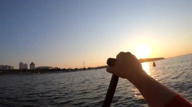 Şafak vakti SUP sörf tahtasında yüzen bir adam. Beyaz SUP tahtasının üzerinde yüzen ve günbatımında kıyıya yakın dalgalarla kürek çeken insanlar. Aktif yaşam tarzı eğlence sporu POV
