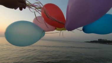 Alacakaranlıkta deniz kıyısında renkli balonlarla oynayan biri. Gün batımında deniz sahilinde bir sürü renkli balon elinde. Çok renkli balonlar kurdeleyle bağlanmış. Yavaş çekim