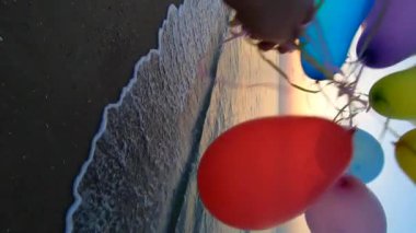 Alacakaranlıkta deniz kıyısında renkli balonlarla oynayan biri. Gün batımında deniz sahilinde bir sürü renkli balon elinde. Çok renkli balonlar kurdele bağladı. Ağır çekim. Dikey