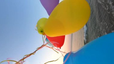 Deniz kıyısında renkli balonlarla oynayan bir adam var. Gün batımında deniz sahilinde bir sürü renkli balon elinde. Çok renkli balonlar kurdeleyle bağlanmış. Ağır çekim. Dikey