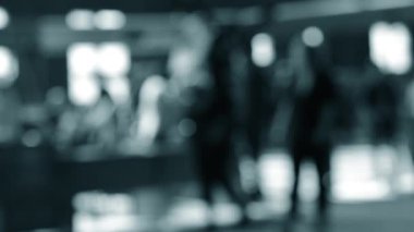 Arka plan bulanık. Birçok insan gün boyunca pencereli büyük bir odanın içinde yürür. Siyah siluetler, insanlar. Mavi beyaz siyah renk