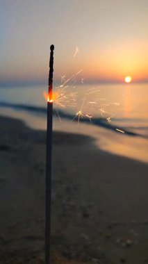 Gün batımının şafağında deniz kıyısındaki kumsalda yanan ve parlayan Bengal ateş maytabı. Denizde Bengal ışığı. Noel 'i kutlayan yeni yıl partisini kutlayalım.