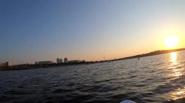 Güneş doğarken ya da batarken şehrin kıyısında SUP 'de yüzen bir kadın. Sabahları ya da akşamları denizdeki SUP sörf tahtasında kürek çeken biri. Bakış açısı. Dinlen, tatil turizmi.