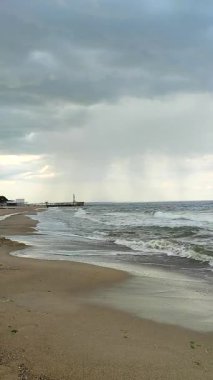 Yağmur fırtınası ve kumlu sahil kıyıları. Kara fırtına bulutları, yağmur, deniz yüzeyi ve kumlu sahil. Doğa. Doğal arka plan. Fırtınalı hava. Denizde fırtına. Dikey