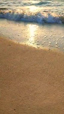 Beyaz köpüklü deniz dalgaları kumlu sahil kıyısında yuvarlanıyor. Deniz kıyısındaki sarı kumdaki açık mavi deniz dalgalarının görüntüsü. Deniz Burnu. Deniz manzarası. Kıyı manzarası Doğa Doğal arka plan Dikey