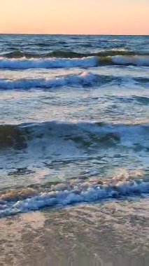 Beyaz köpüklü deniz dalgaları kumlu sahil kıyısında yuvarlanıyor. Deniz kıyısındaki sarı kumdaki açık mavi deniz dalgalarının görüntüsü. Deniz Burnu. Deniz manzarası. Kıyı manzarası Doğa Doğal arka plan Dikey