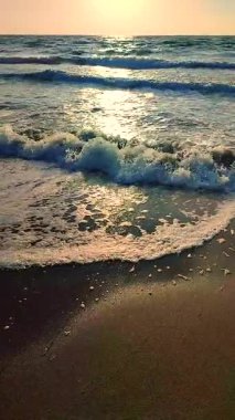 Beyaz köpüklü deniz dalgaları kumlu sahil kıyısında yuvarlanıyor. Deniz kıyısındaki sarı kumdaki açık mavi deniz dalgalarının görüntüsü. Deniz Burnu. Deniz manzarası. Kıyı manzarası Doğa Doğal arka plan Dikey