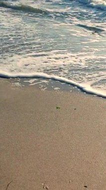 Beyaz köpüklü deniz dalgaları kumlu sahil kıyısında yuvarlanıyor. Deniz kıyısındaki sarı kumdaki açık mavi deniz dalgalarının görüntüsü. Deniz Burnu. Deniz manzarası. Kıyı manzarası Doğa Doğal arka plan Dikey