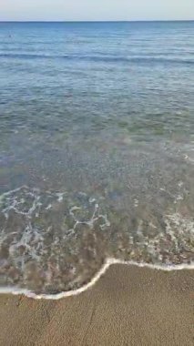 Güzel deniz manzarası. Deniz manzarası. Sakin güneşli bir günde, deniz kıyısındaki kumsalda akan temiz şeffaf suyla mavi deniz ve deniz dalgalarının görüntüsü. Hiç kimse. Doğa. Doğal arka plan. Dikey