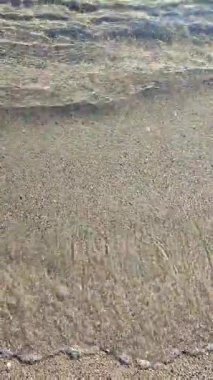 Güneşli bir günde, deniz kıyısının kumlu sahilinde güzel, şeffaf, küçük deniz dalgaları. Temiz su, güneş parlaması ve yakın plan kumlu zeminde gölgeler. Doğal soyut arka plan. Dikey