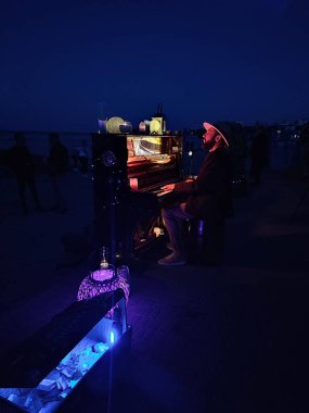 Odessa, Ukrayna, 25 Mayıs 2024: Piyanist deniz kenarında arka planda piyano çalıyor ve yaz gecesi onu dinleyen birçok kişi var. Seyircilerle piyano çalan müzisyen konseri.