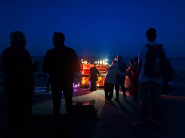 Piyanist deniz kenarında arka planda piyano çalıyor ve birçok insan yaz gecesi onu dinliyor. Seyircilerle piyano çalan müzisyen konseri.