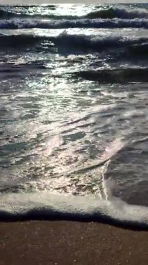 Beyaz köpüklü deniz dalgaları kumlu sahil kıyısında yuvarlanıyor. Deniz kıyısındaki sarı kumdaki açık mavi deniz dalgalarının görüntüsü. Deniz Burnu. Deniz manzarası. Kıyı manzarası Doğa Doğal arka plan Dikey