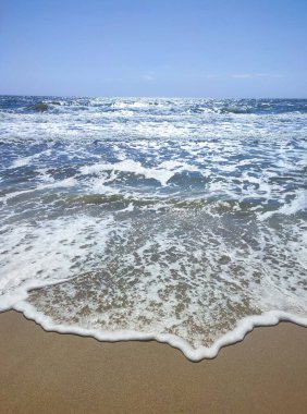 Beyaz köpüklü, şeffaf deniz dalgaları ve güneşli bir yaz gününde kumlu sahil sahilinde mavi gökyüzü. Deniz kıyısında. Kumsal. Doğa Doğal arkaplan